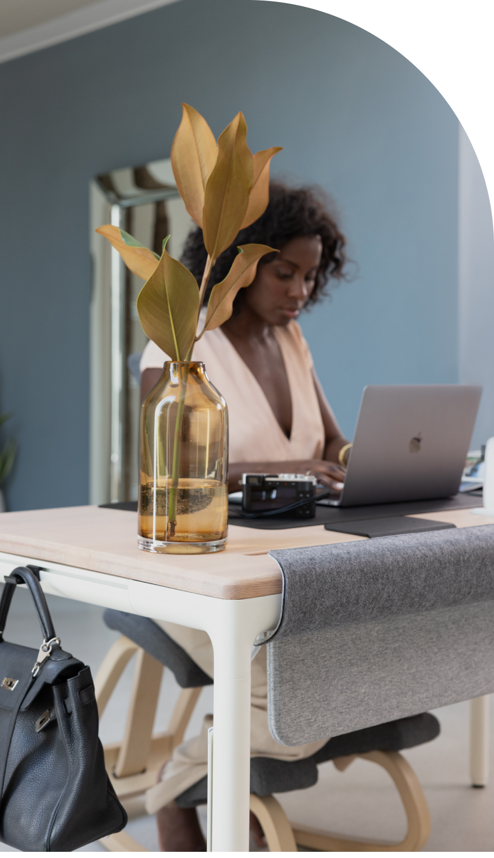 A woman works at a laptop while sitting at the Tenon desk from Beflo