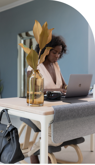 A woman works at a laptop while sitting at the Tenon desk from Beflo