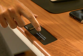 Person using a touchscreen on a beflo Tenon desk with a phone and keyboard in the background.