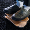 Person wearing insulated shoes with The North Face logo with a wood beflo strata footrest on a dark textured surface