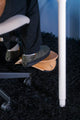 Person sitting on a chair with feet resting on a beflo wooden footrest in a dark room.