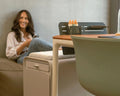 Woman sitting on a couch next to a beflo desk with a chair in a home office setting.