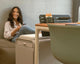 Woman sitting on a couch next to a beflo desk with a chair in a home office setting.