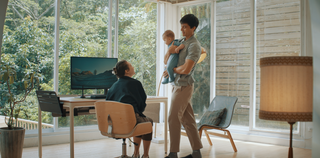 A person in the process of handing a baby to another person seated at a Tenon desk