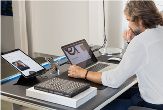 A man sots and uses a laptop at a Tenon desk