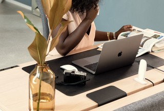 A woman reads a magazine while seated at a Tenon desk