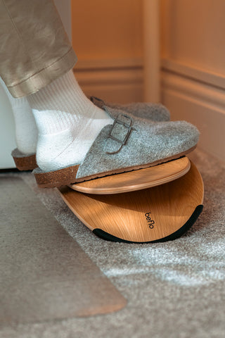Person wearing gray slippers with wooden sole on a bathroom floor.